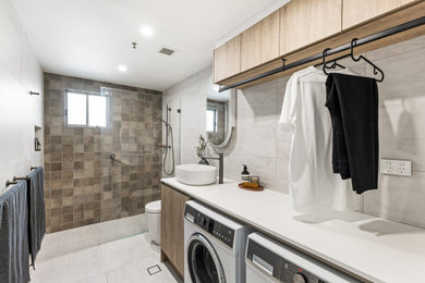 Photo of a mid-sized contemporary single-wall utility room in Sydney with a single-bowl sink, flat-panel cabinets, medium wood cabinets, grey splashback, grey walls, a side-by-side washer and dryer, grey floor and white benchtop.