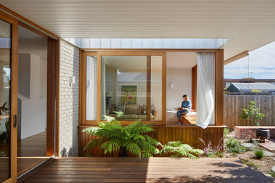 Small contemporary backyard and ground level deck in Melbourne with with privacy feature and a roof extension.