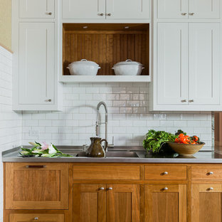 Design ideas for a large traditional u-shaped kitchen pantry in Boston with an integrated sink, shaker cabinets, white cabinets, stainless steel benchtops, white splashback, subway tile splashback, stainless steel appliances, medium hardwood floors, with island and brown floor.