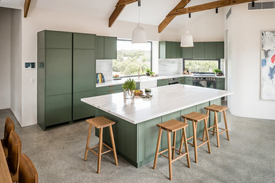 Large contemporary l-shaped open plan kitchen in Melbourne with a farmhouse sink, shaker cabinets, green cabinets, marble benchtops, white splashback, marble splashback, black appliances, concrete floors, with island, grey floor and white benchtop.