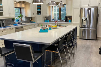 Example of a large transitional l-shaped vinyl floor, gray floor and exposed beam eat-in kitchen design in Toronto with an undermount sink, shaker cabinets, blue cabinets, quartzite countertops, gray backsplash, stainless steel appliances, an island, white countertops and glass tile backsplash