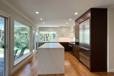 Inspiration for a mid-sized modern l-shaped medium tone wood floor and yellow floor open concept kitchen remodel in San Francisco with an undermount sink, flat-panel cabinets, brown cabinets, quartz countertops, white backsplash, quartz backsplash, stainless steel appliances, an island and white countertops