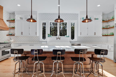 This is an example of a large country u-shaped open plan kitchen in Other with a farmhouse sink, beaded inset cabinets, white cabinets, quartz benchtops, white splashback, subway tile splashback, stainless steel appliances, light hardwood floors, with island, brown floor and white benchtop.