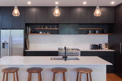 Large l-shaped eat-in kitchen in Newcastle - Maitland with with island, a double-bowl sink, flat-panel cabinets, dark wood cabinets, white splashback, subway tile splashback, stainless steel appliances, medium hardwood floors and white benchtop.