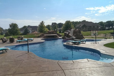 This is an example of a large backyard custom-shaped pool in Minneapolis with a water feature and stamped concrete.