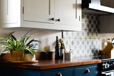 Design ideas for a large traditional l-shaped kitchen/diner in Essex with a double-bowl sink, shaker cabinets, blue cabinets, granite worktops, black appliances, porcelain flooring, an island, brown floors and black worktops.
