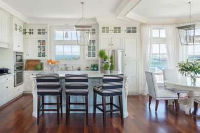 Design ideas for a mid-sized beach style eat-in kitchen in Providence with recessed-panel cabinets, white cabinets, marble benchtops, white splashback, ceramic splashback, stainless steel appliances, medium hardwood floors and with island.