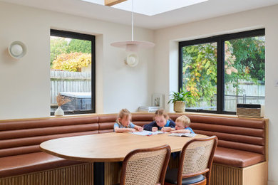This is an example of a medium sized modern dining room in London with banquette seating, white walls and a feature wall.