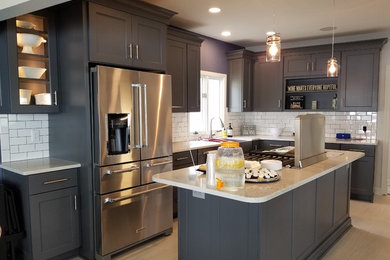 Large contemporary l-shaped kitchen pantry in Milwaukee with a farmhouse sink, recessed-panel cabinets, grey cabinets, granite benchtops, white splashback, ceramic splashback, stainless steel appliances, ceramic floors, with island, multi-coloured floor and multi-coloured benchtop.