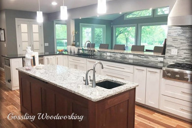 Mid-sized contemporary u-shaped kitchen in Burlington with granite benchtops, grey splashback, glass tile splashback, stainless steel appliances and light hardwood floors.