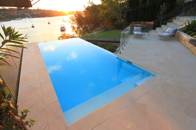 This is an example of a contemporary backyard rectangular infinity pool in Sydney with natural stone pavers.