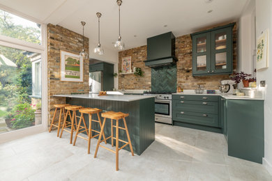 Design ideas for a medium sized contemporary l-shaped kitchen/diner in London with a belfast sink, shaker cabinets, green cabinets, quartz worktops, green splashback, ceramic splashback, stainless steel appliances, porcelain flooring, an island, beige floors, white worktops and feature lighting.