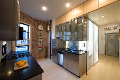 Kitchen - mid-sized industrial galley light wood floor and brown floor kitchen idea in New York with an undermount sink, flat-panel cabinets, stainless steel cabinets, glass sheet backsplash, stainless steel appliances and no island