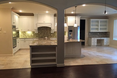Eat-in kitchen - mid-sized traditional l-shaped travertine floor and beige floor eat-in kitchen idea in Houston with an undermount sink, raised-panel cabinets, white cabinets, granite countertops, beige backsplash, stone tile backsplash, stainless steel appliances and an island