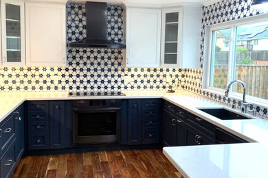 This is an example of a transitional u-shaped eat-in kitchen in San Francisco with recessed-panel cabinets, blue cabinets, marble benchtops, blue splashback, mosaic tile splashback, medium hardwood floors, no island, brown floor and white benchtop.
