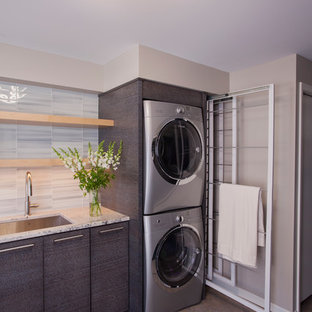 ミネアポリスの中サイズのモダンスタイルのおしゃれなランドリールーム (アンダーカウンターシンク、フラットパネル扉のキャビネット、グレーのキャビネット、御影石カウンター、ラミネートの床、上下配置の洗濯機・乾燥機、マルチカラーの床、グレーの壁) の写真