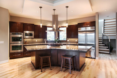 Example of a trendy l-shaped eat-in kitchen design in Portland with an undermount sink, flat-panel cabinets, dark wood cabinets, granite countertops, gray backsplash, glass tile backsplash and stainless steel appliances
