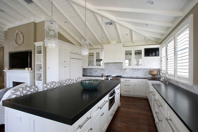 Inspiration for a mid-sized traditional u-shaped open plan kitchen in Tampa with a farmhouse sink, beaded inset cabinets, white cabinets, granite benchtops, grey splashback, stone tile splashback, panelled appliances, dark hardwood floors and with island.