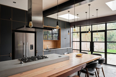 Photo of a medium sized industrial galley kitchen/diner in London with a double-bowl sink, flat-panel cabinets, black cabinets, concrete worktops, brown splashback, wood splashback, slate flooring, an island, multi-coloured floors, grey worktops, exposed beams and feature lighting.