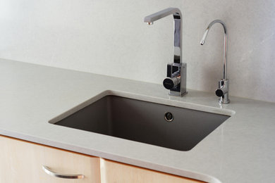 Ejemplo de cocina lineal moderna grande cerrada sin isla con fregadero bajoencimera, armarios con paneles lisos, puertas de armario de madera clara, encimera de cuarzo compacto, salpicadero verde, electrodomésticos de acero inoxidable, suelo de baldosas de porcelana, suelo gris y encimeras grises