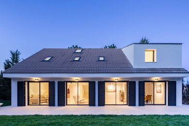 Cette image montre une façade de maison blanche minimaliste en stuc de taille moyenne et à un étage avec un toit à deux pans, un toit en tuile et un toit gris.
