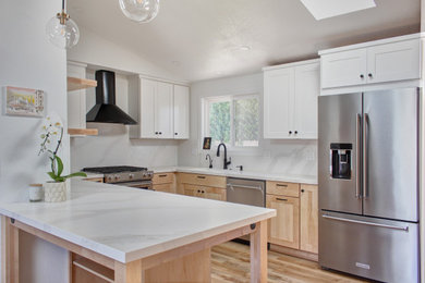 Example of a mid-sized danish u-shaped light wood floor, brown floor and vaulted ceiling eat-in kitchen design in Other with an undermount sink, shaker cabinets, light wood cabinets, quartz countertops, white backsplash, quartz backsplash, stainless steel appliances, a peninsula and white countertops