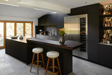Large contemporary single-wall open plan kitchen in London with flat-panel cabinets, black cabinets, engineered stone countertops, black splashback, engineered quartz splashback, black appliances, an island and black worktops.