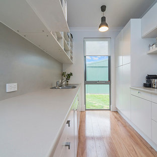 Small contemporary kitchen pantry ideas - Inspiration for a small contemporary galley medium tone wood floor kitchen pantry remodel in Adelaide with a single-bowl sink, flat-panel cabinets, white cabinets, laminate countertops, gray backsplash, stone slab backsplash, stainless steel appliances and no island