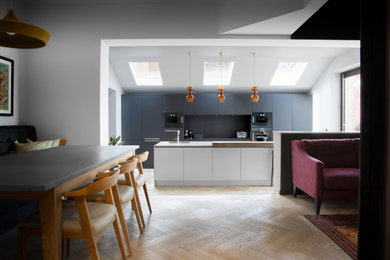 This is an example of a large scandi galley open plan kitchen in Cheshire with an integrated sink, flat-panel cabinets, black cabinets, quartz worktops, black splashback, black appliances, light hardwood flooring, an island and white worktops.