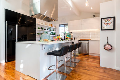 Mid-sized contemporary l-shaped eat-in kitchen in Auckland with an undermount sink, quartz benchtops, yellow splashback, subway tile splashback, black appliances, medium hardwood floors and with island.