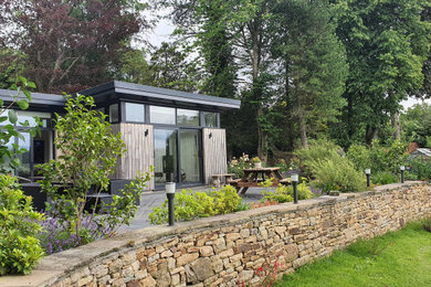 This is an example of a small contemporary bungalow front tiny house in Other with wood cladding, a flat roof, a green roof and board and batten cladding.