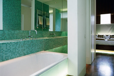 Inspiration for a small contemporary master bathroom in London with glass-front cabinets, tile benchtops, a drop-in tub, a curbless shower, green tile, mosaic tile, white walls and medium hardwood floors.