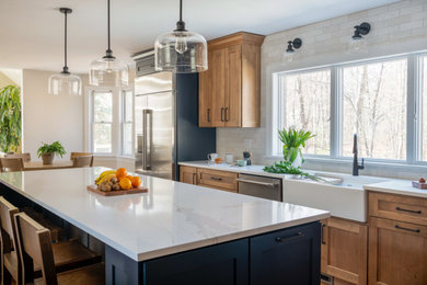Large transitional l-shaped medium tone wood floor and blue floor eat-in kitchen photo in Boston with a double-bowl sink, shaker cabinets, medium tone wood cabinets, quartz countertops, white backsplash, porcelain backsplash, stainless steel appliances, an island and white countertops