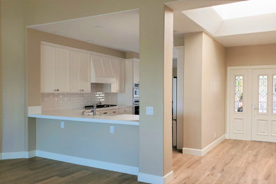 Eat-in kitchen - small transitional u-shaped porcelain tile eat-in kitchen idea in Orange County with a farmhouse sink, shaker cabinets, white cabinets, quartzite countertops, white backsplash, subway tile backsplash, white appliances and white countertops