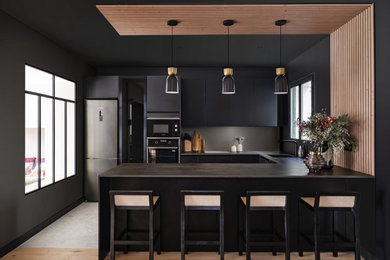 Cette photo montre une cuisine ouverte encastrable et noire et bois tendance en U de taille moyenne avec un évier encastré, un placard à porte plane, des portes de placard noires, un plan de travail en stratifié, une crédence noire, sol en béton ciré, îlot, un sol gris, plan de travail noir et fenêtre au-dessus de l'évier.