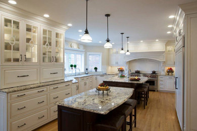 Eat-in kitchen - large traditional u-shaped medium tone wood floor and brown floor eat-in kitchen idea in Montreal with an undermount sink, raised-panel cabinets, white cabinets, granite countertops, white backsplash, porcelain backsplash, stainless steel appliances and two islands
