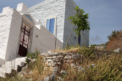 This is an example of a small mediterranean two-storey blue exterior in Other with stone veneer, a butterfly roof, a tile roof and a red roof.