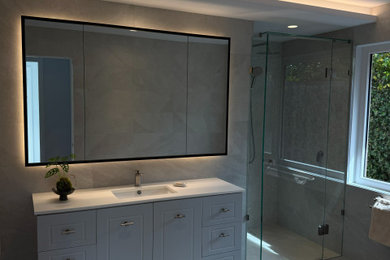 Mid-sized contemporary master bathroom in Melbourne with grey cabinets, a drop-in tub, an alcove shower, gray tile, porcelain tile, ceramic floors, an undermount sink, solid surface benchtops, a hinged shower door, white benchtops, a niche, a single vanity and a freestanding vanity.