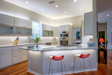 Large trendy medium tone wood floor eat-in kitchen photo in Tampa with flat-panel cabinets, white cabinets, quartz countertops, white backsplash, porcelain backsplash, stainless steel appliances and a peninsula