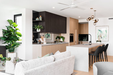 This is an example of a mid-sized contemporary l-shaped kitchen in Brisbane with an undermount sink, flat-panel cabinets, light wood cabinets, mirror splashback, stainless steel appliances, light hardwood floors, with island, beige floor and white benchtop.