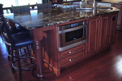 Example of a classic l-shaped medium tone wood floor enclosed kitchen design in Calgary with an undermount sink, raised-panel cabinets, dark wood cabinets, soapstone countertops, beige backsplash, ceramic backsplash, stainless steel appliances and an island