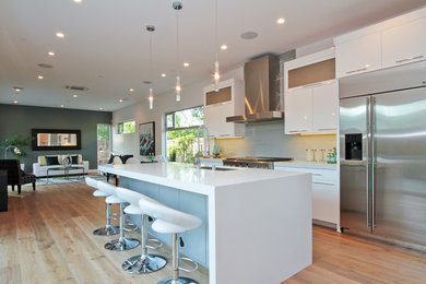 Open concept kitchen - contemporary single-wall light wood floor open concept kitchen idea in New Orleans with an undermount sink, flat-panel cabinets, white cabinets, solid surface countertops, blue backsplash, ceramic backsplash, stainless steel appliances and an island