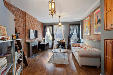 Example of a mid-sized minimalist open concept medium tone wood floor living room design in New York with gray walls, a standard fireplace, a stone fireplace and a wall-mounted tv