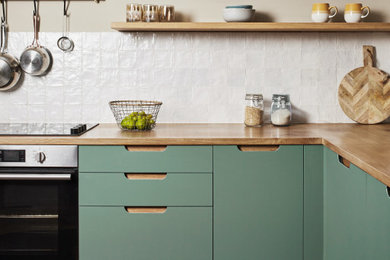 This is an example of a medium sized modern u-shaped open plan kitchen in Devon with flat-panel cabinets, green cabinets, wood worktops, white splashback, stone tiled splashback, integrated appliances, medium hardwood flooring and a breakfast bar.