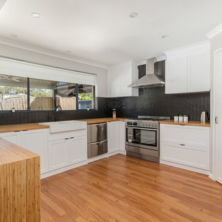 This is an example of a large traditional u-shaped kitchen pantry in Perth with a farmhouse sink, shaker cabinets, white cabinets, wood benchtops, black splashback, mosaic tile splashback, stainless steel appliances, bamboo floors, no island, brown floor and brown benchtop.