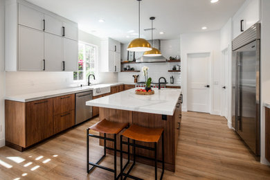 Example of a mid-sized 1950s u-shaped laminate floor and beige floor open concept kitchen design in San Diego with a farmhouse sink, flat-panel cabinets, medium tone wood cabinets, marble countertops, white backsplash, ceramic backsplash, stainless steel appliances, an island and white countertops