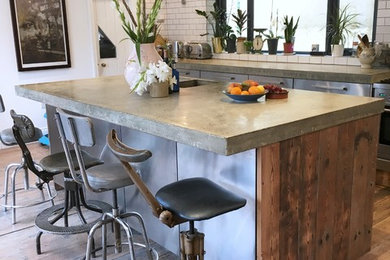 Medium sized eclectic kitchen/diner in London with a double-bowl sink, flat-panel cabinets, stainless steel cabinets, concrete worktops, white splashback, ceramic splashback, stainless steel appliances, light hardwood flooring, a breakfast bar and brown floors.
