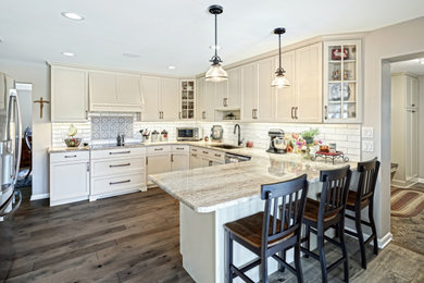 Inspiration for a mid-sized transitional l-shaped medium tone wood floor and beige floor eat-in kitchen remodel in Other with a double-bowl sink, shaker cabinets, beige cabinets, granite countertops, beige backsplash, travertine backsplash, stainless steel appliances, a peninsula and beige countertops
