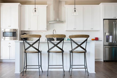 Mid-sized cottage galley medium tone wood floor and brown floor open concept kitchen photo in Seattle with a farmhouse sink, recessed-panel cabinets, white cabinets, solid surface countertops, white backsplash, subway tile backsplash, stainless steel appliances and an island