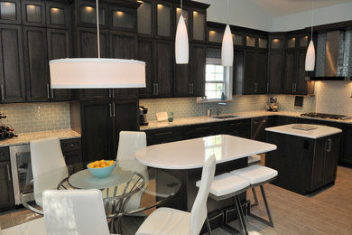 Large urban galley ceramic tile enclosed kitchen photo in St Louis with an integrated sink, raised-panel cabinets, dark wood cabinets, solid surface countertops, blue backsplash, glass tile backsplash, stainless steel appliances and two islands